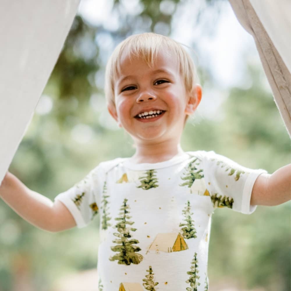 Baby boy holding open a tent entrance wearing the Camping Bamboo Short Sleeve One Piece by Milkbarn Kids