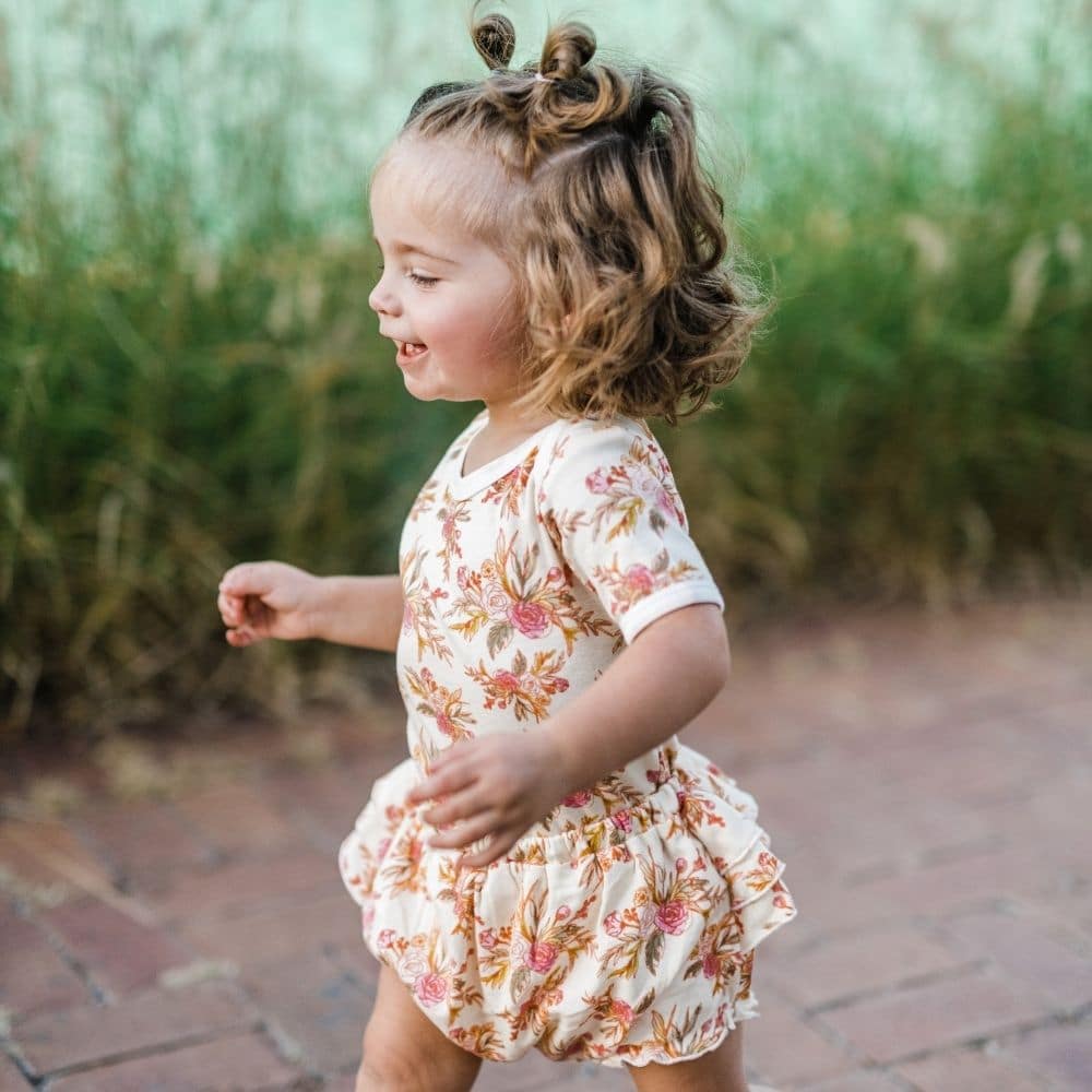 Baby girl walking on a brick path wearing Vintage Floral Organic Ruffle Bloomer by Milkbarn Kids