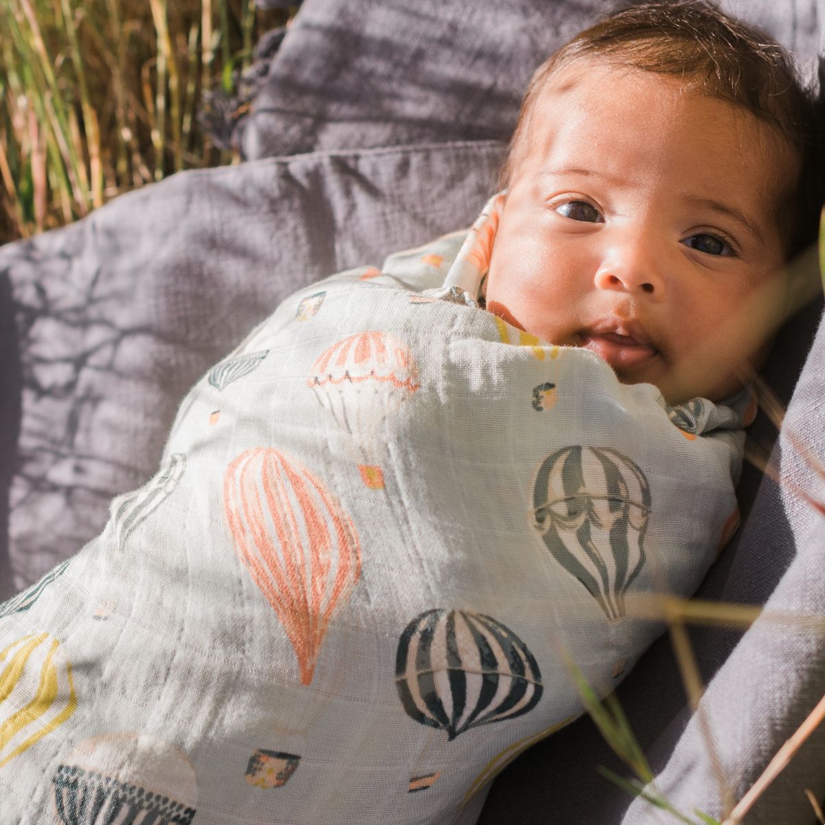 Baby resting in a field wrapped in the Vintage Balloons Muslin Swaddle Blanket by Milkbarn