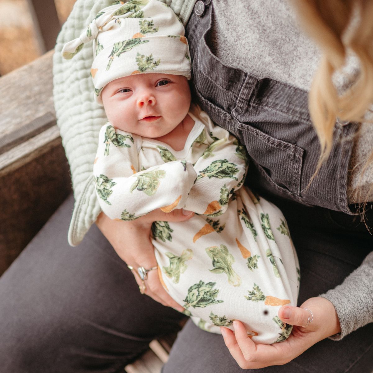 Mom and Newborn Baby cradled in arms wearing the organic cotton and bamboo newborn baby gown and hat set in the fresh veggies print by Milkbarn