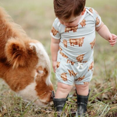 Baby boy with a baby cow wearing the Highland Cow Bamboo Pocket Bloomer and short sleeve One Piece by Milkbarn Kids