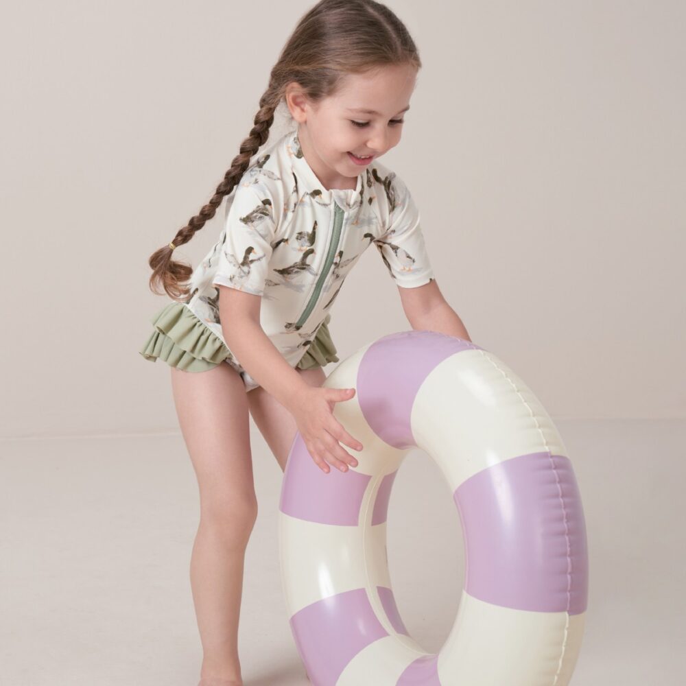 Toddler girl playing with a round pool floatie wearing the Duck Zipper Short Sleeve Ruffle Leg Swimsuit