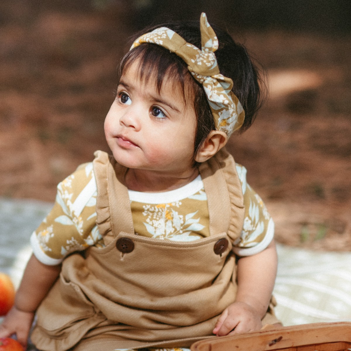 Baby girl sitting on a picnic blanket wearing the Gold Floral organic cotton Knotted Headband by Milkbarn