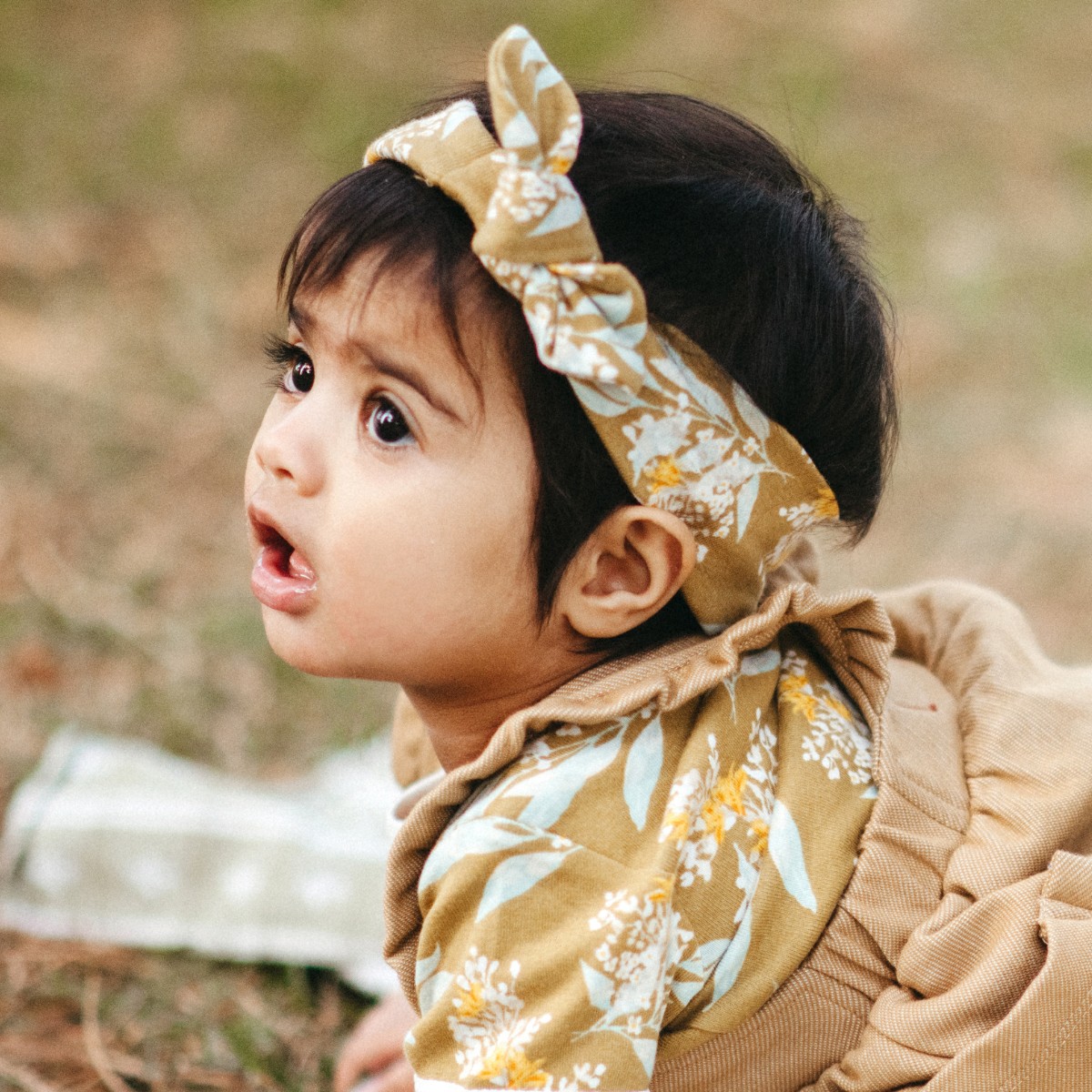Baby girl crawling on a picnic blanket wearing the Gold Floral organic cotton Knotted Headband by Milkbarn