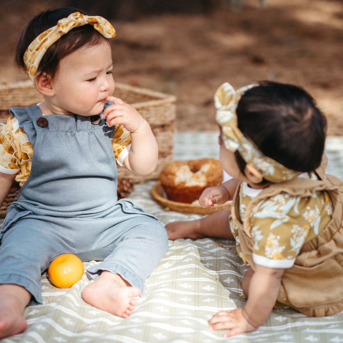 Baby girls outside having a picnic wearing the Honeycomb Bamboo Knotted Headband and the Gold Floral Organic Knotted Headband by Milkbarn
