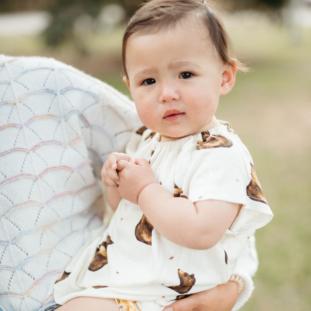 Baby girl being held in her mother's arms while wearing the bamboo Honey Bear Dress top and Honeycomb bamboo Bloomers by Milkbarn
