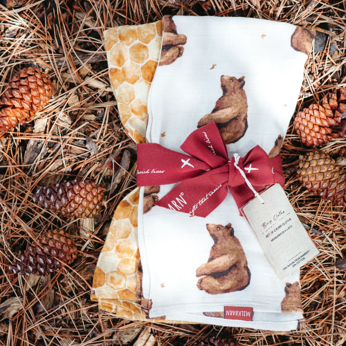 Displayed on a bed of pinecones are the Honey Bear and Honeycomb Burp Cloths Packaged and wrapped in Milkbarns ribbon