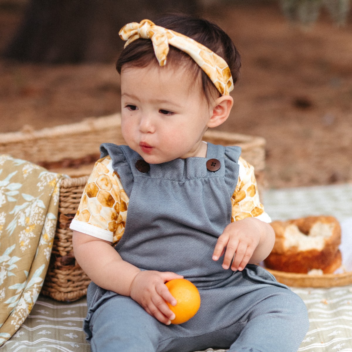 Baby girl outside having a picnic wearing the Honeycomb Bamboo Knotted Headband by Milkbarn