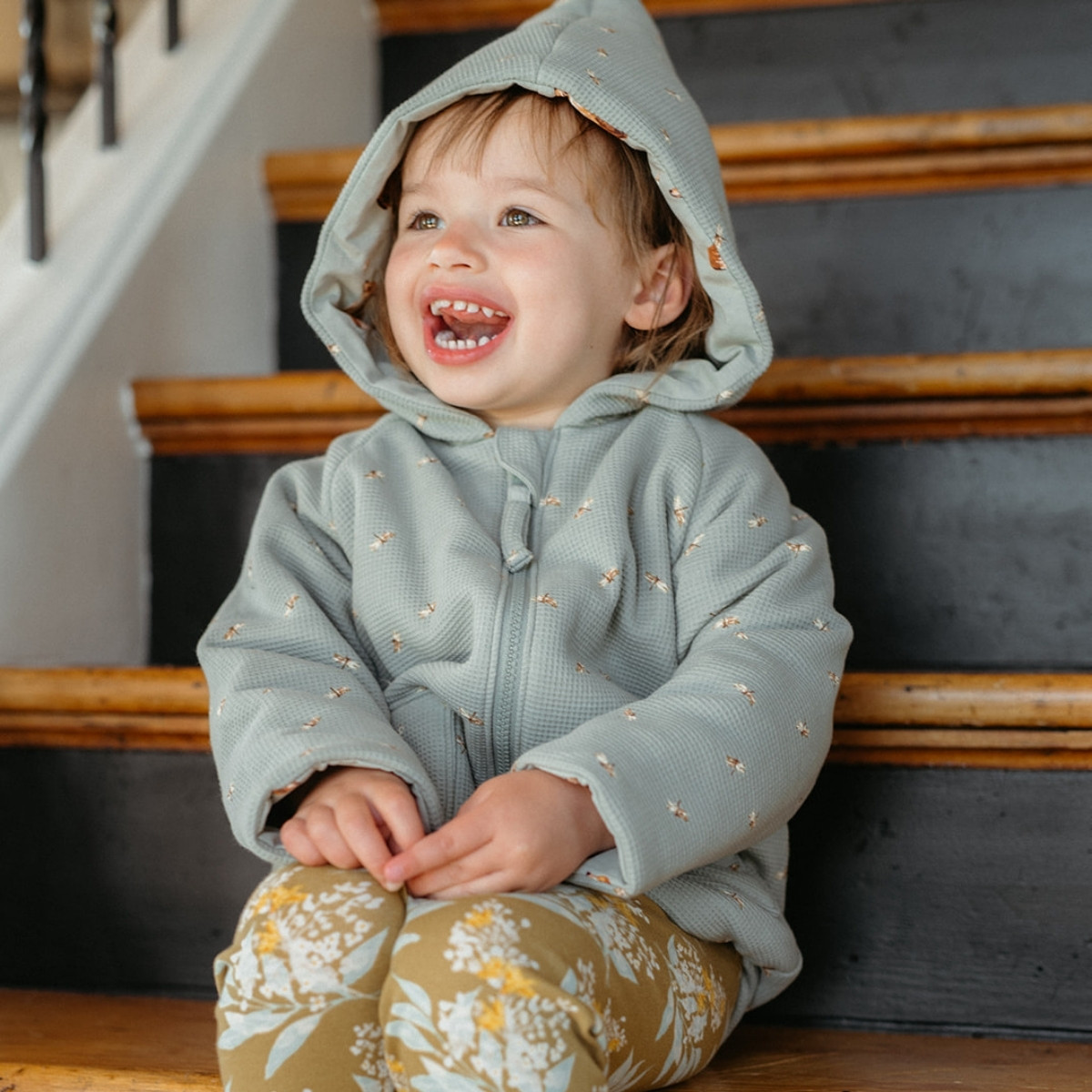 Little girl sitting on wooden steps wearing the Dragonfly and Fox Reversible Waffle Knit Hooded Jacket