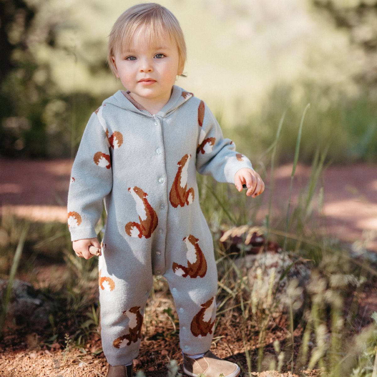 Baby boy outside under the trees wearing the knitted cashmere and cotton hooded jumpsuit in the fox pattern by milkbarn