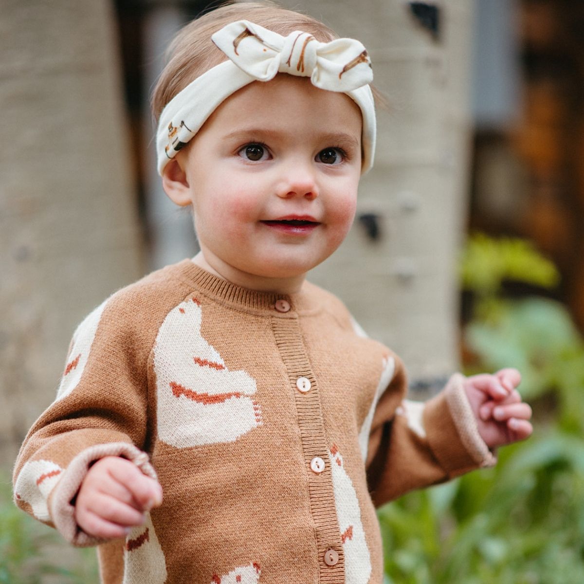 Toddler outside wearing the Honey Bear Knitted Birdseye Jacquard Cardigan and coordinating honey bear headband