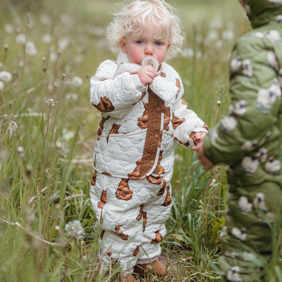 Baby and toddle in a green field of dandelions wearing the honey bear quilted jacket, scarf and pants.